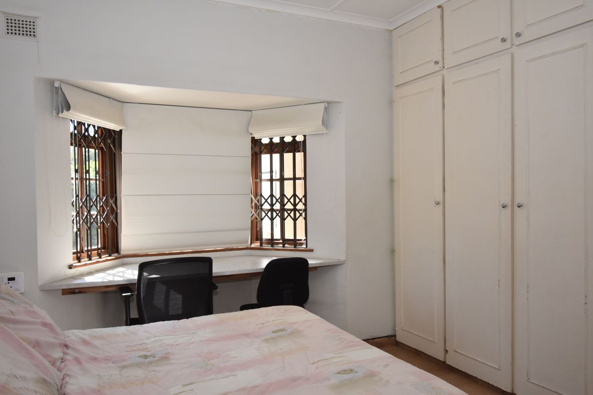Bedroom featuring built-in cupboards, a bay window with a built-in desk, and security gates on the windows.