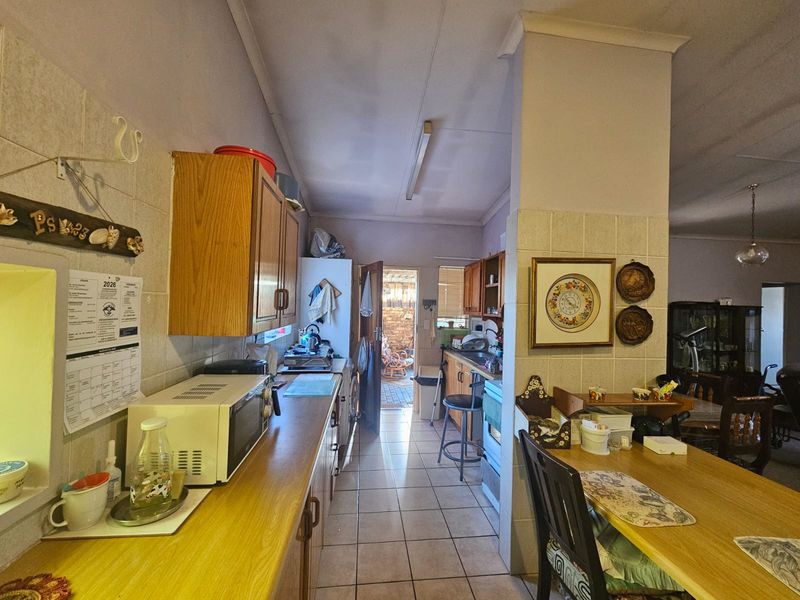 A functional kitchen featuring wooden cabinetry, laminate countertops, and tiled flooring, with a direct layout leading to an exterior doorway.
