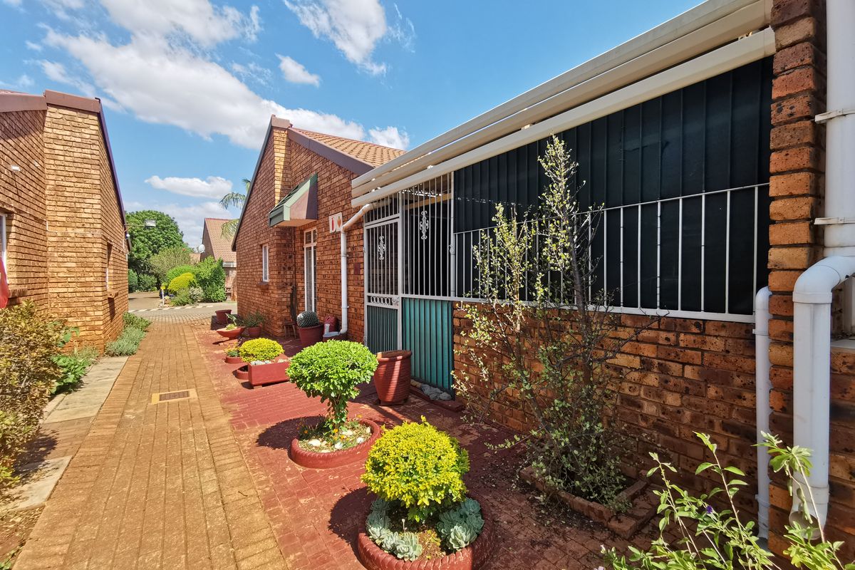 A side view of a face brick townhouse featuring a paved walkway, security gates, and established garden beds along the exterior wall.