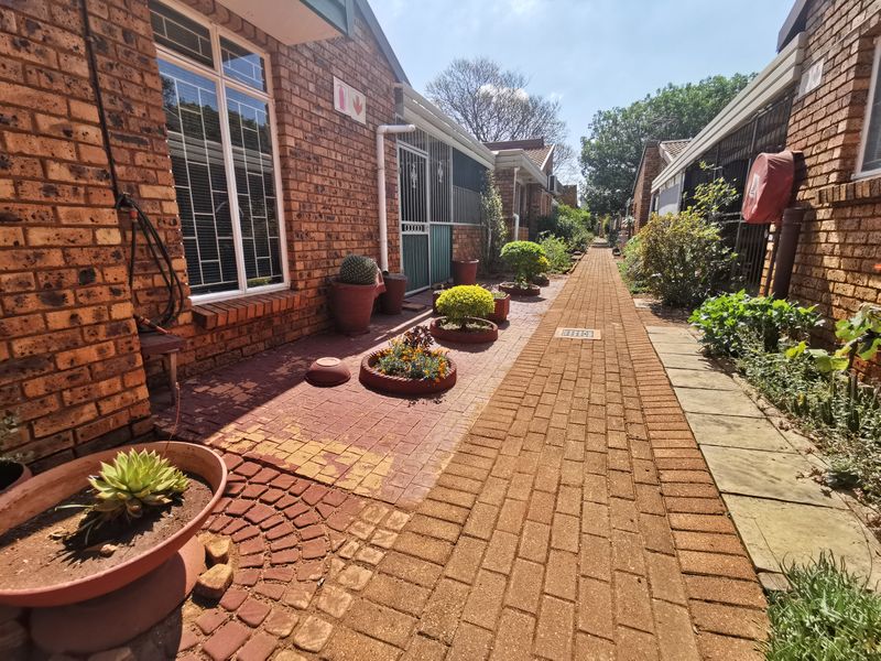 A paved exterior walkway between townhouse units featuring facebrick walls, security gates, and established garden beds.