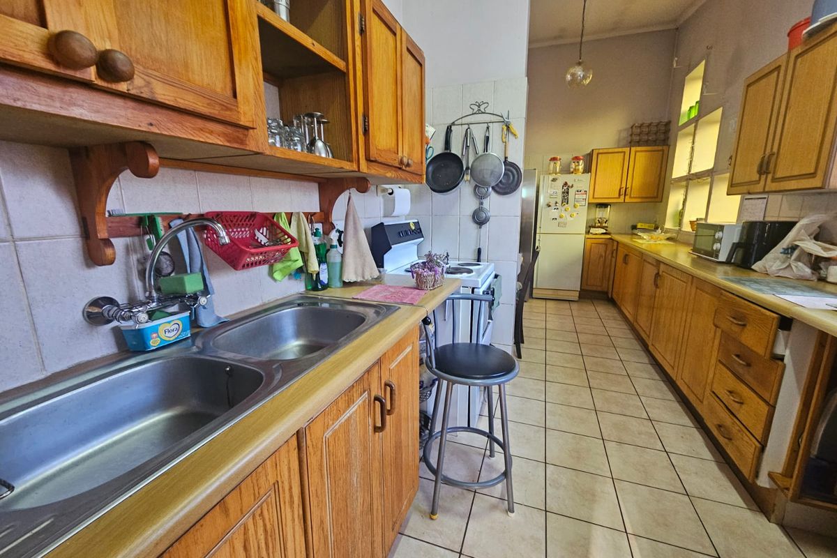 A functional kitchen featuring extensive wooden cabinetry, a double stainless steel sink, tiled flooring, and a freestanding stove with a tiled backsplash.