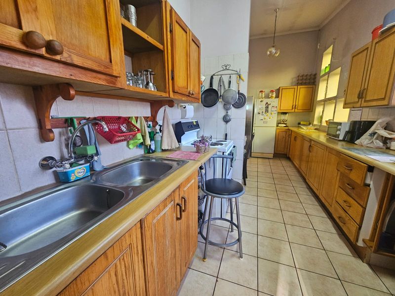 A functional kitchen featuring extensive wooden cabinetry, a double stainless steel sink, tiled flooring, and a freestanding stove with a tiled backsplash.