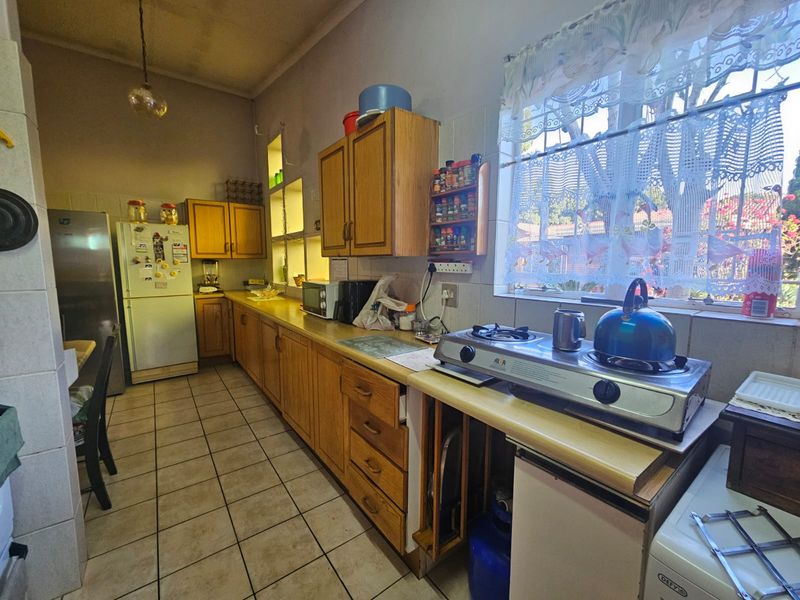 A functional kitchen featuring wooden cabinetry, laminate countertops, tiled flooring, and a gas hob, offering a dated aesthetic ready for modernization.