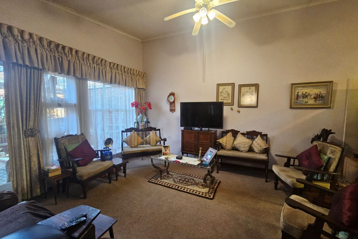 A spacious living room featuring high ceilings, a central ceiling fan, and large windows that provide ample natural light.