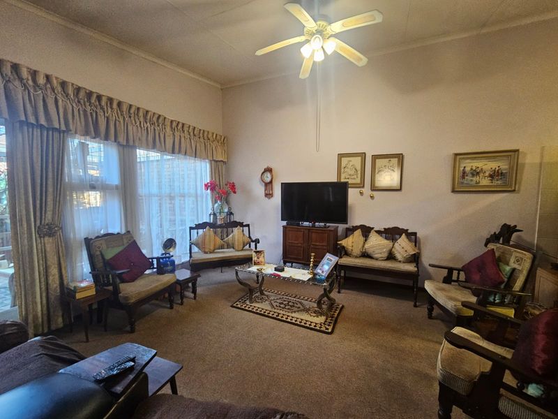 A spacious living room featuring high ceilings, a central ceiling fan, and large windows that provide ample natural light.