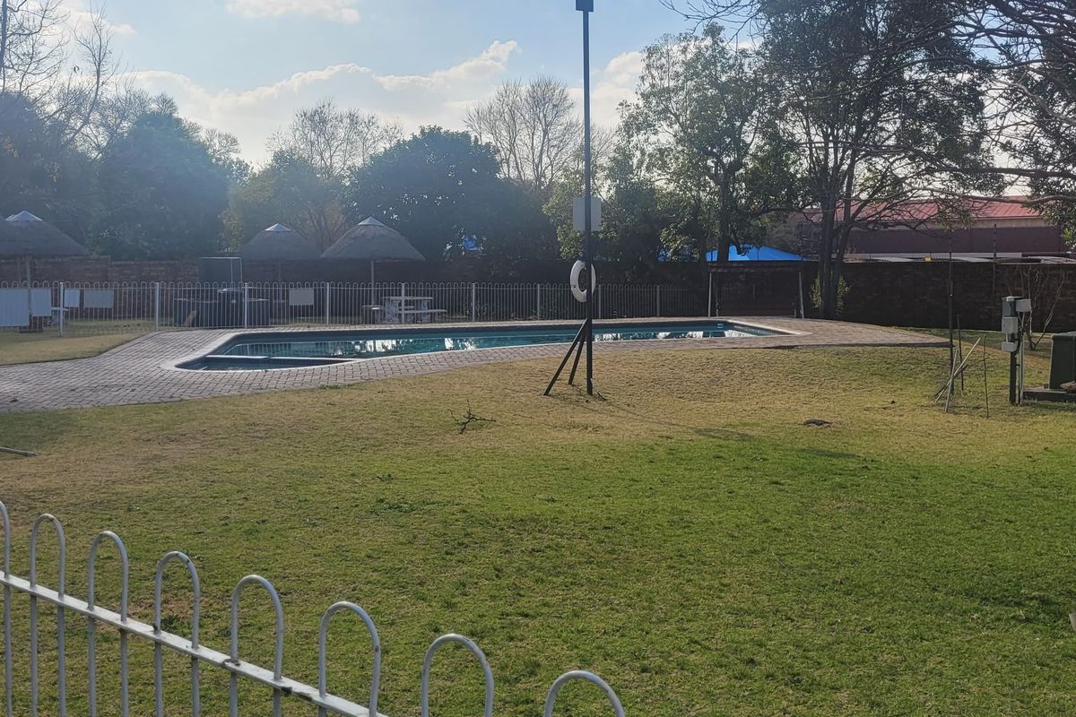 Communal pool area featuring a swimming pool, paved surround, and thatch umbrellas set within a fenced garden space.