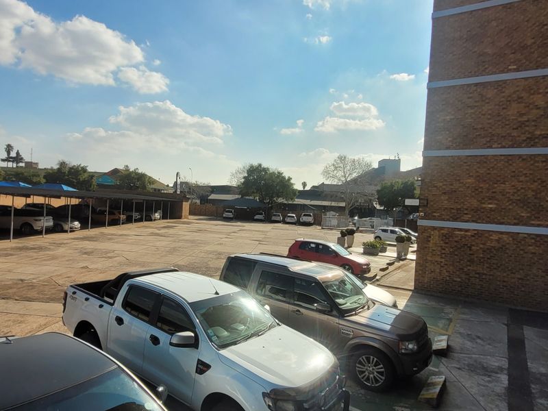 View of the apartment complex exterior, featuring a paved parking area with covered bays and brick building facade.