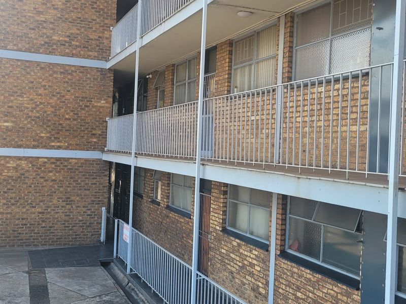 Exterior view of a multi-story flat complex featuring face brick construction, external walkways with metal balustrades, and paved ground level access.