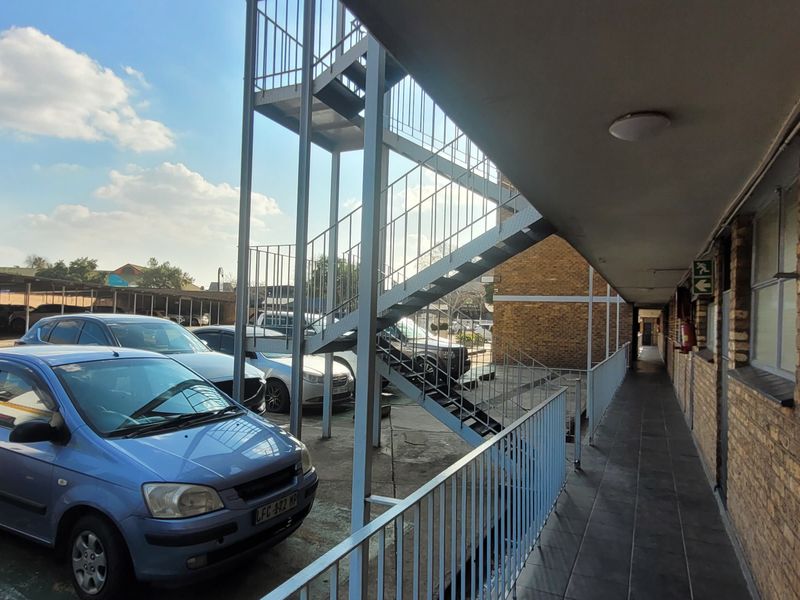 Exterior view of a flat complex featuring a metal staircase, brick facade, and a covered walkway overlooking the parking area.