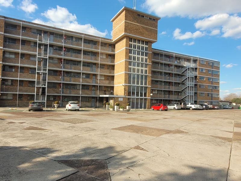 Front elevation of a multi-story brick apartment building featuring a large concrete parking area and covered parking bays.