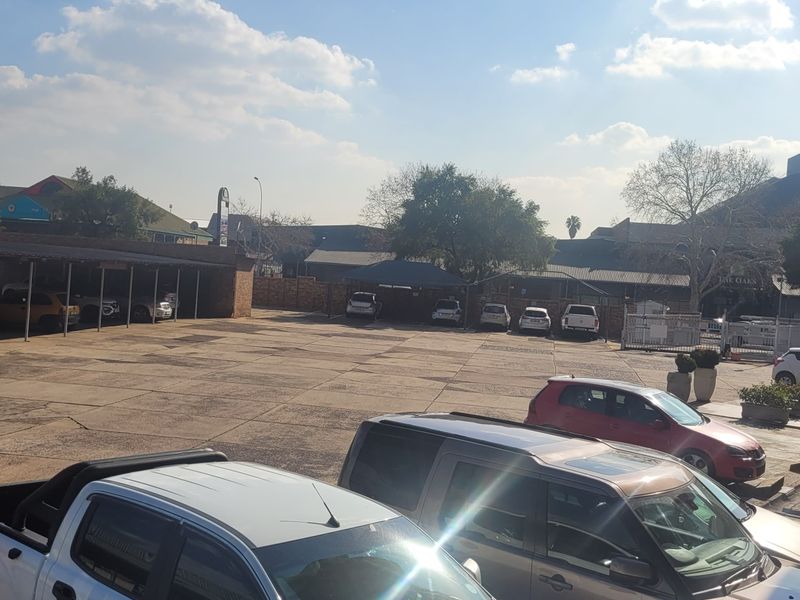 An outdoor paved parking area featuring covered carport structures and brick building facades.