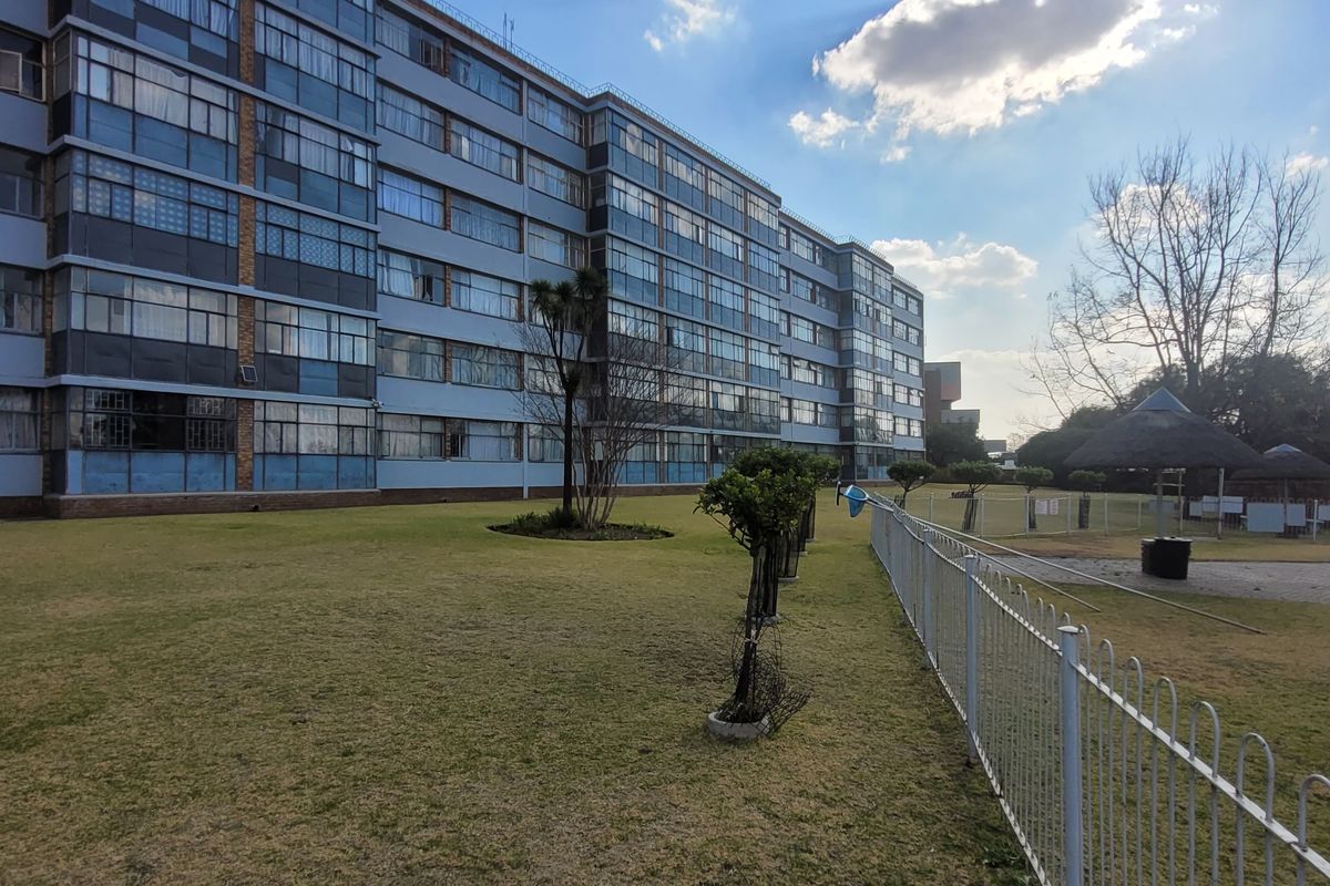 View of the rear residential building facade featuring a communal lawn, swimming pool area, and thatched lapa structures.