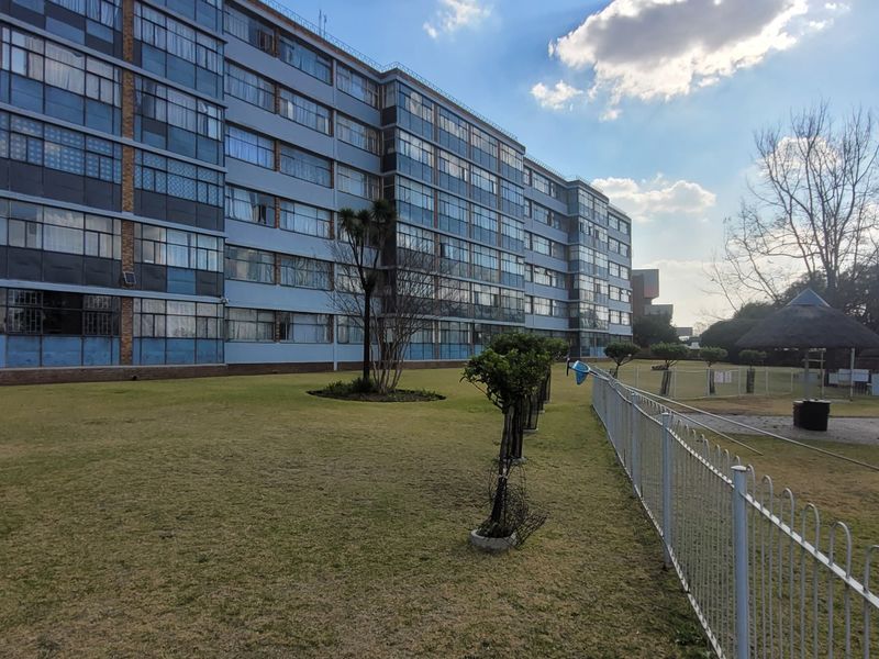 View of the rear residential building facade featuring a communal lawn, swimming pool area, and thatched lapa structures.