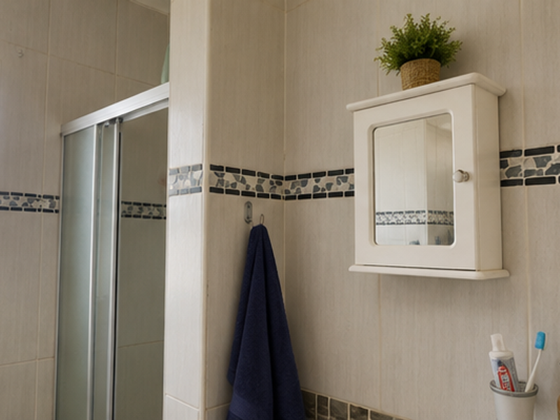 A functional bathroom featuring a shower enclosure, tiled walls with decorative border, and a wall-mounted medicine cabinet.
