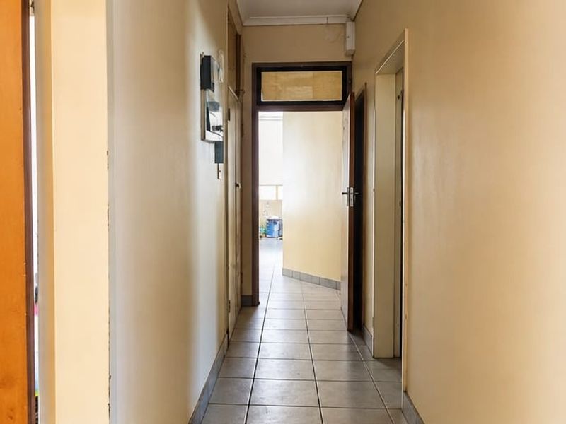 A functional hallway featuring tiled flooring and access to multiple rooms, showing signs of wear and dated finishes.