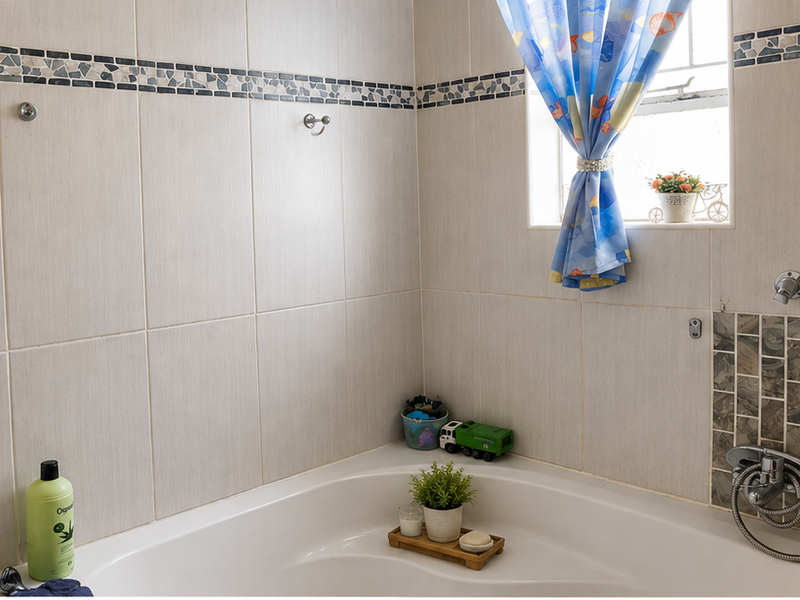 A bathroom featuring a corner bathtub with tiled walls, a decorative mosaic border, and chrome fixtures.