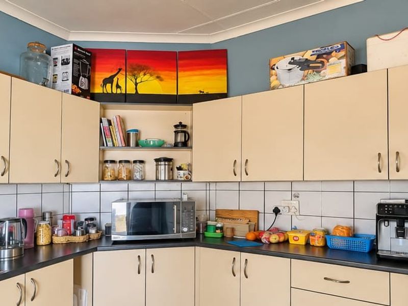 A functional kitchen featuring light-toned laminate cabinetry, dark countertops, and a classic white ceramic tile backsplash.