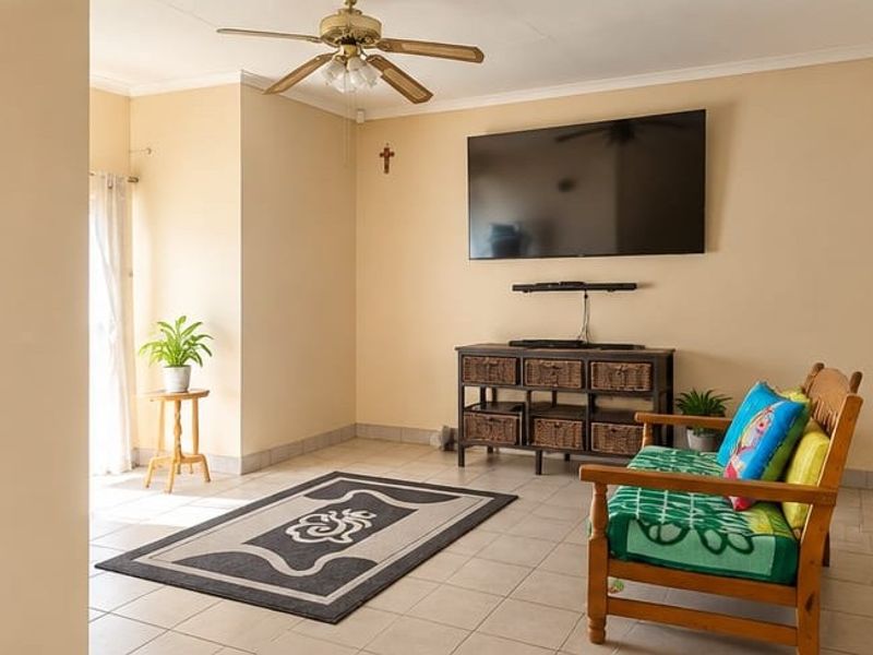 A bright living room featuring neutral walls, tiled flooring, and a ceiling fan, offering a comfortable and functional space.