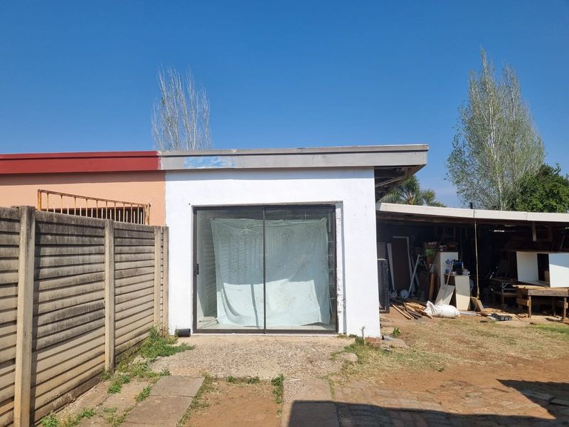Rear exterior view showing a sliding glass door entrance, concrete patio area, and adjacent covered outdoor space with a precast boundary wall.