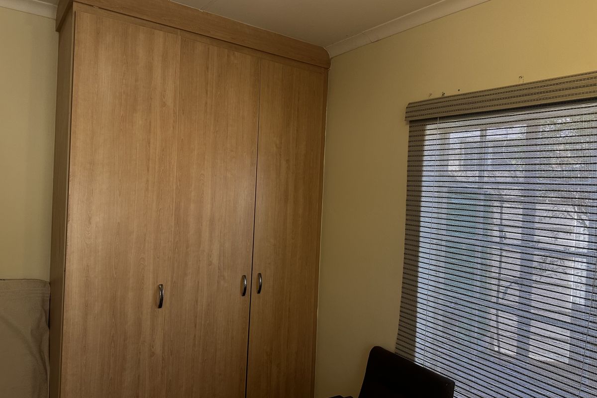 A bedroom featuring a full-height built-in wooden wardrobe and a window fitted with a roller blind.