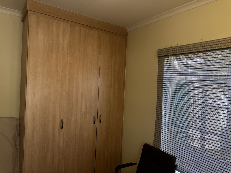 A bedroom featuring a full-height built-in wooden wardrobe and a window fitted with a roller blind.