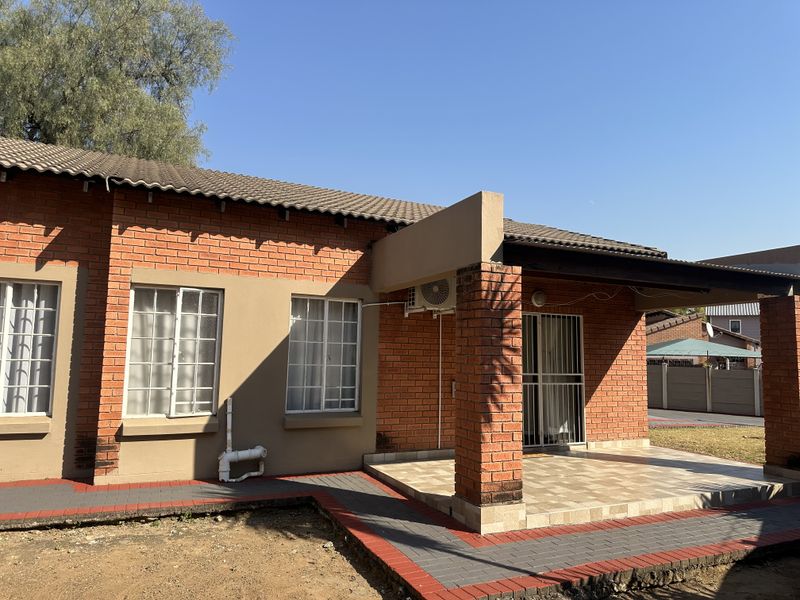 Rear view of a brick house featuring a covered patio, paved walkways, and an installed air conditioning unit.