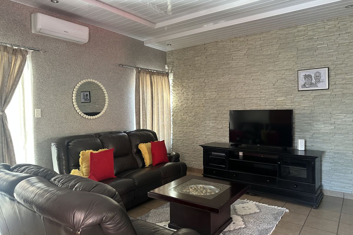A comfortable living room featuring a textured stone accent wall, tiled flooring, and a split-system air conditioner for climate control.