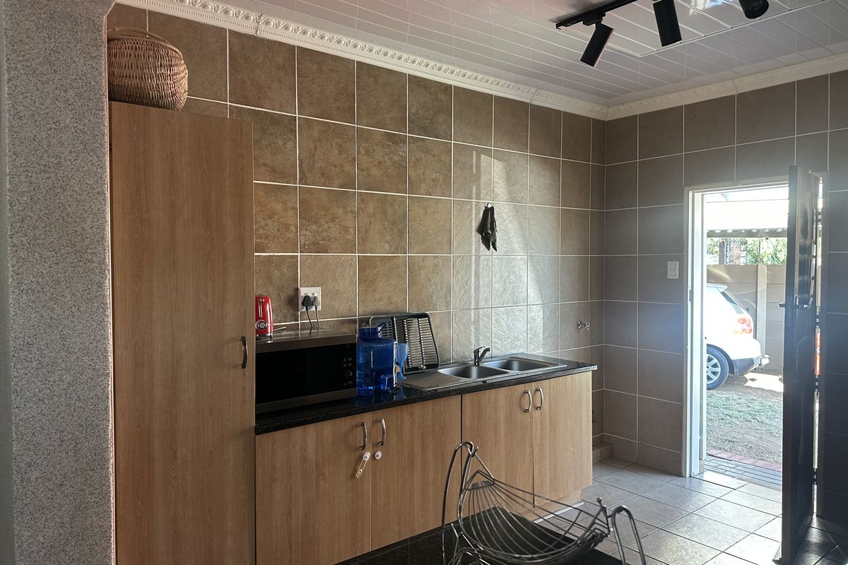 A functional kitchen area featuring built-in cabinetry, a double sink, tiled splashbacks, and modern track lighting with direct access to the exterior.