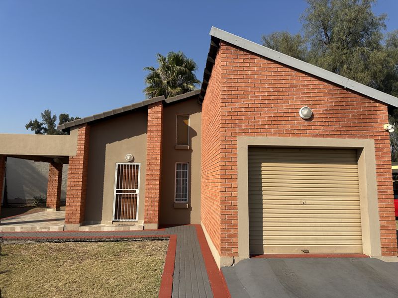 Front elevation of a brick house featuring a single roller garage door, a paved walkway, and a covered patio area.