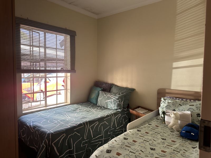 A compact bedroom featuring a window with a blind and visible ceiling water staining, requiring maintenance.