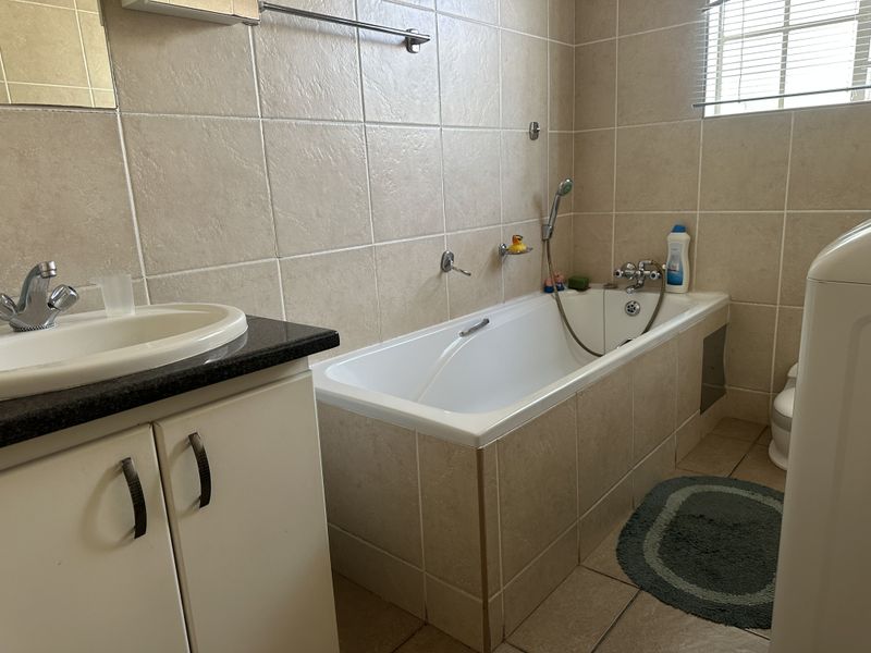 A functional bathroom featuring a tiled bathtub with handheld shower mixer, a vanity with a drop-in basin, and neutral wall and floor tiling.