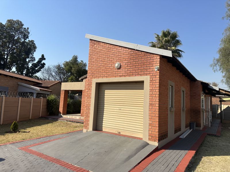 A detached brick garage featuring a roller shutter door and a paved driveway, situated on a residential property.
