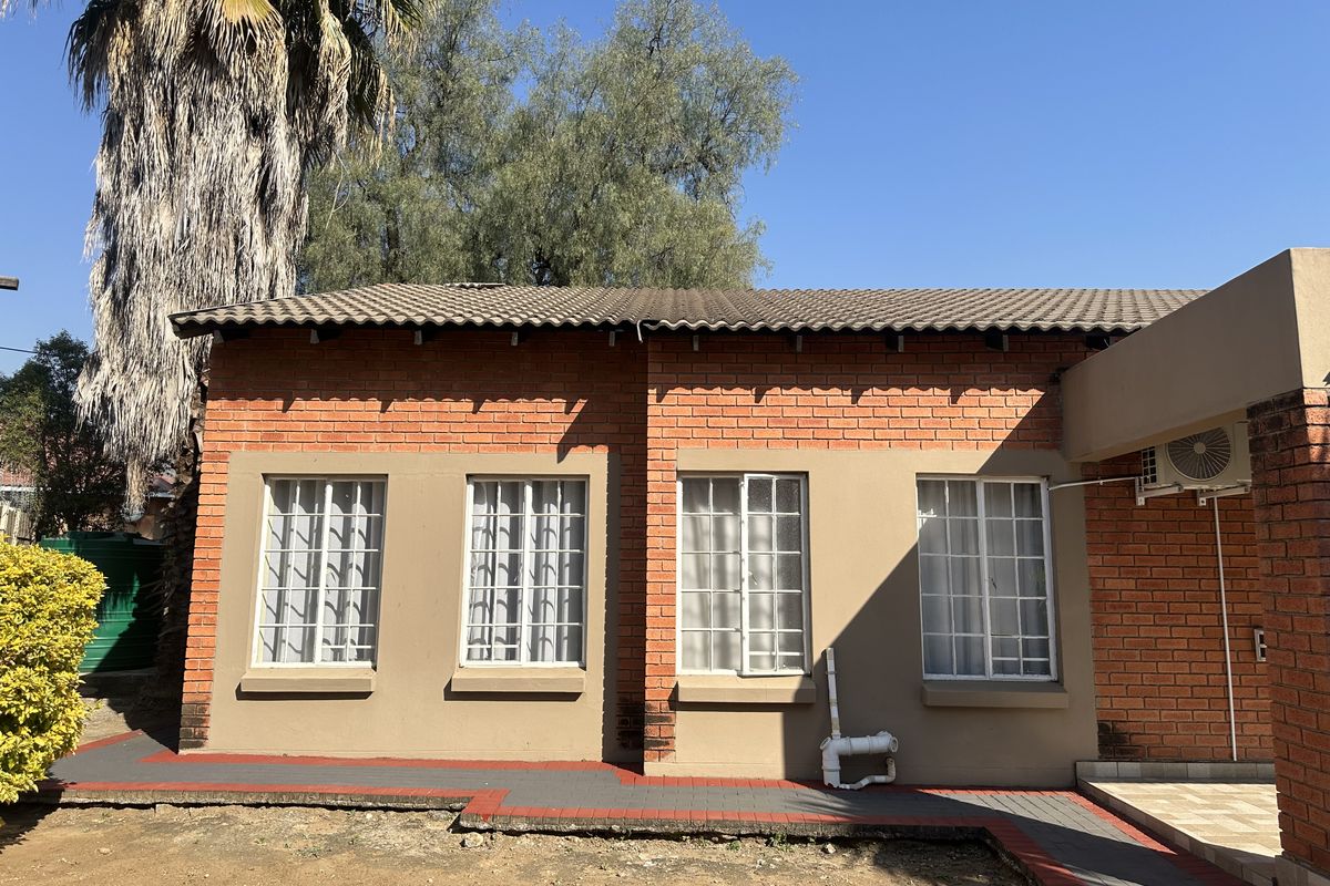 Rear exterior view of a face brick house featuring a tiled roof, security-barred windows, and a paved walkway.