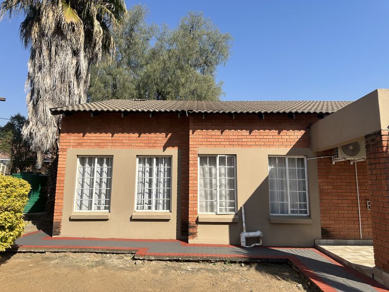 Rear exterior view of a face brick house featuring a tiled roof, security-barred windows, and a paved walkway.