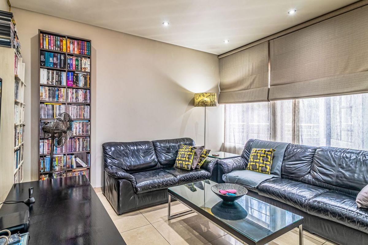 A comfortable living room featuring tiled flooring, recessed downlighting, and large windows fitted with neutral roman blinds.