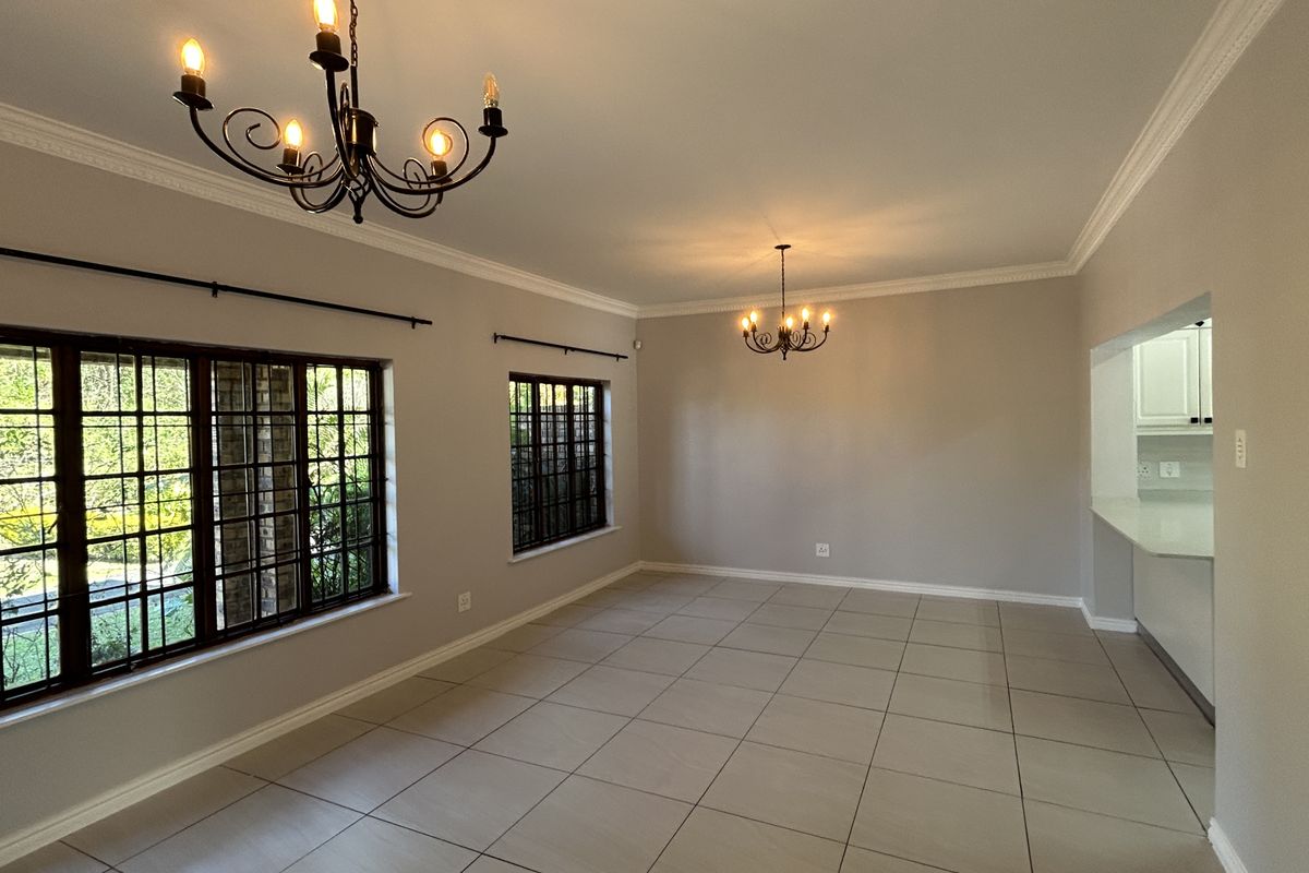 Spacious, light-filled living area featuring neutral tiled flooring, elegant wrought iron chandeliers, crown molding, and secure window bars, offering a versatile open-plan layout.