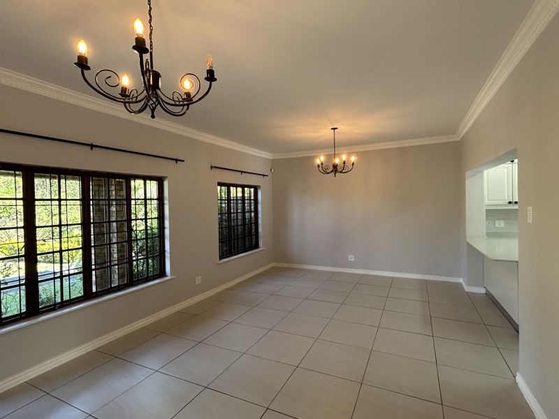 Spacious, light-filled living area featuring neutral tiled flooring, elegant wrought iron chandeliers, crown molding, and secure window bars, offering a versatile open-plan layout.