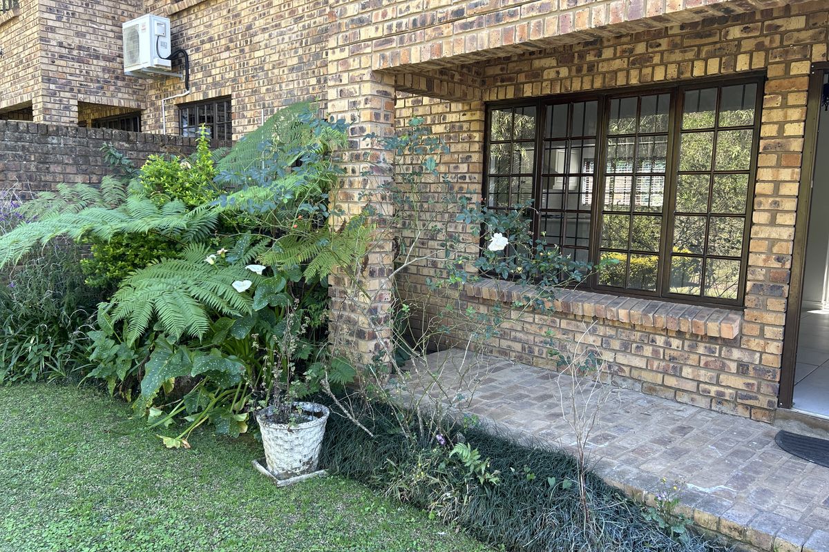 A rear exterior view of the townhouse featuring a face brick facade, a paved patio area, and established garden landscaping.