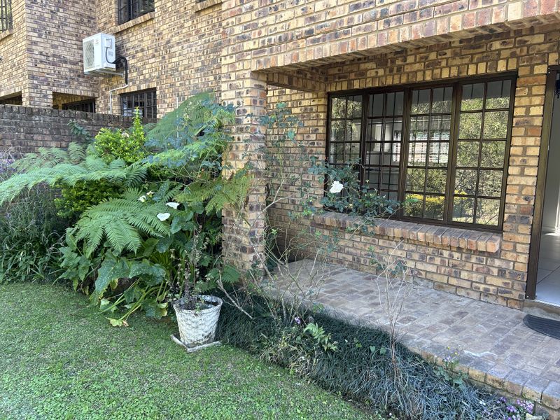 A rear exterior view of the townhouse featuring a face brick facade, a paved patio area, and established garden landscaping.