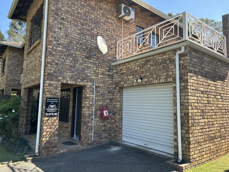 Front elevation of a face brick townhouse featuring a single garage, a balcony with metal railings, and a covered entrance area.