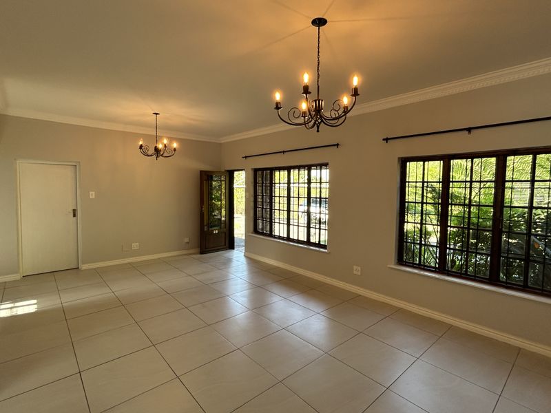 Spacious, light-filled living area featuring neutral tiled flooring, decorative cornicing, and classic wrought iron chandeliers, offering a clean canvas for interior design.