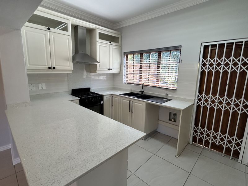 Modern kitchen featuring white cabinetry, quartz countertops, a stainless steel extractor fan, double sink, and tiled flooring with a secure entrance door.