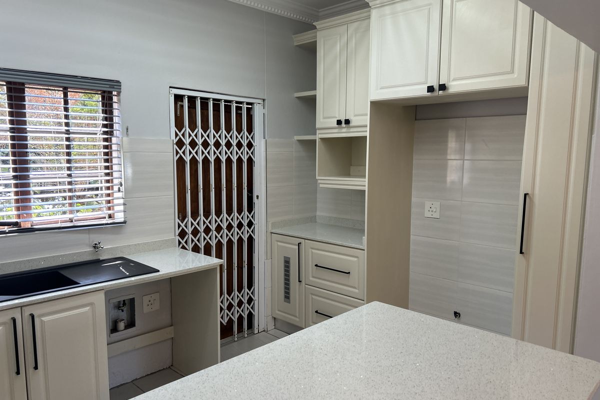 A clean, modern kitchen featuring white cabinetry, quartz countertops, a tiled backsplash, and a secure entrance door with a security gate.