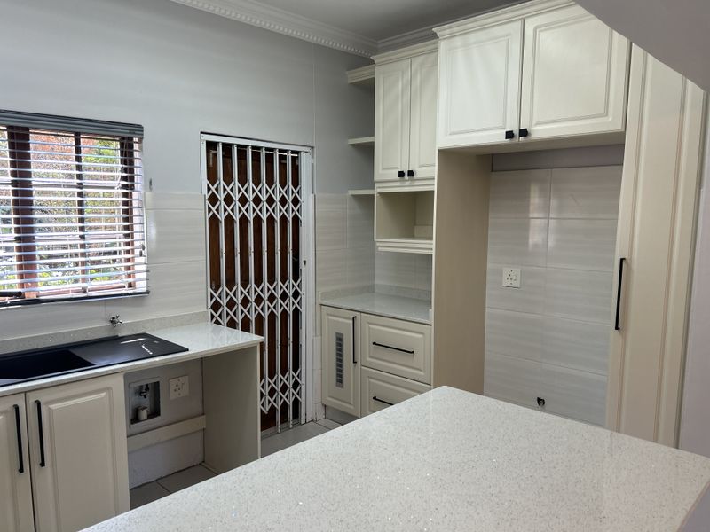 A clean, modern kitchen featuring white cabinetry, quartz countertops, a tiled backsplash, and a secure entrance door with a security gate.
