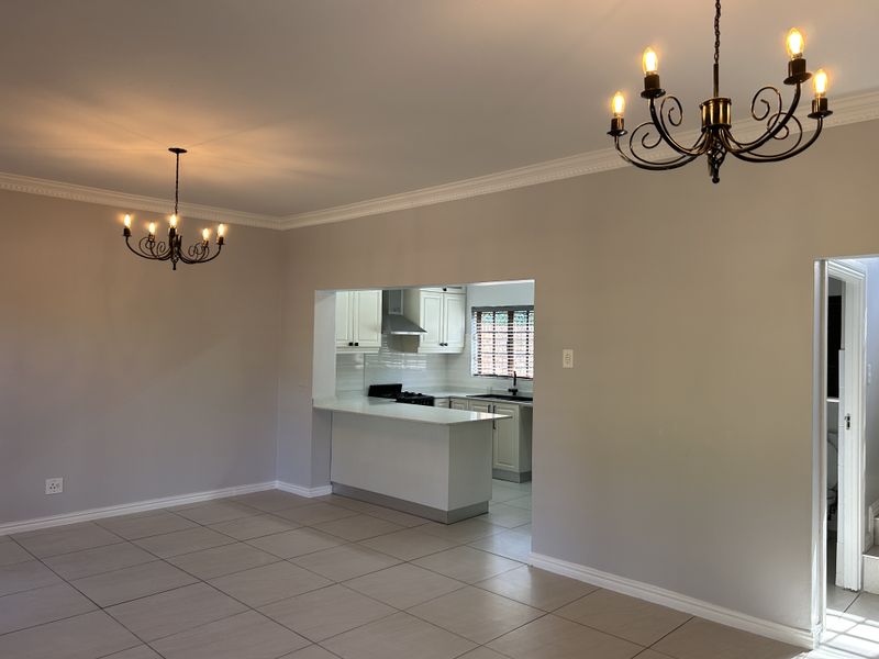 Spacious open-plan living and dining area featuring neutral tiled flooring, crown molding, and a functional kitchen with built-in cabinetry and appliances.