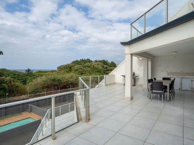 Spacious covered balcony featuring tiled flooring, glass balustrades, and built-in cabinetry, offering scenic views and an ideal space for outdoor entertaining.