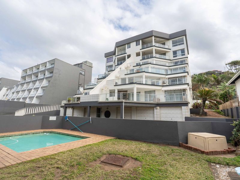 Rear view of the apartment building featuring multiple balconies, a private swimming pool, and ground-level garage access.
