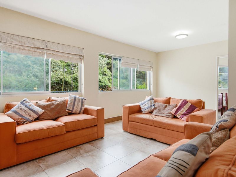 A bright living room featuring neutral tiled flooring, large sliding windows with roman blinds, and a simple flush mount ceiling light.