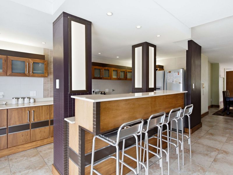 Open plan kitchen featuring wood-finish cabinetry, stone countertops, a breakfast bar with integrated lighting, and tiled flooring throughout the living space.