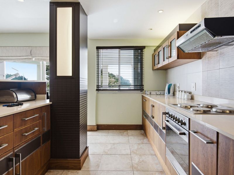 A well-maintained kitchen featuring modern wood-finish cabinetry, stone countertops, integrated appliances, and tiled flooring, offering a functional and clean workspace.